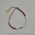 Detail van kralenarmband met rode kralen en een gouden hart hanger op grijs leer - Rood En Roze Afwisselende Parelstijl (1) / 17+3cm