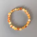 Detail van natuurlijke carneool kralenarmband met gouden tussenstukjes op grijze basis - Rode Carneool Kralenstijl (3)