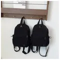 Detail of two black waterproof nylon backpacks hanging on a minimalist white wall hook - Large / Black