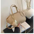 Dettaglio della borsa a secchiello in pelle beige con ciondolo a cuore su tavolo - Cachi