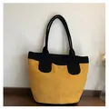 Detalle de un bolso tote grande de ante amarillo con asas negras sobre madera oscura - Talla única / Amarillo