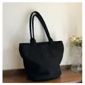 Detalle de bolso tote negro mate con solapas curvas sobre superficie de madera oscura - Talla única / Negro