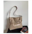 Detailed shot of beige glossy shoulder bag with metal buckles on a black sofa - Khaki