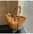 Detail of straw woven tote bag featuring brown leather straps and buckle in natural light - One Size / Khaki