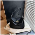 Dettaglio borsa nera in pelle a grana con chiusura dorata su un blazer beige - Con Ciondolo / Nero