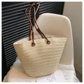 Beigefarbene gewebte Stroh-Shopper-Tasche mit braunen Ledergriffen auf weißem Stuhl - Gebrochenes Weiß