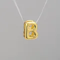 Detalle macro de un colgante letra B burbuja 3D con acabado metálico dorado pulido - Letra B