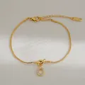 Detail van gouden slangenketting armband met zirkonia cirkel hanger en knoop design - Letter O