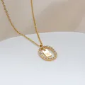 Dettaglio di un ciondolo ovale dorato con strass e lettera W incisa sul metallo - Lettera W