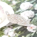 Eleganter Feder-Haarclip aus Gold mit funkelnden Kristallen auf Blumenhintergrund - Blattform / Blattweiß