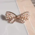 Elegant gold bow hair clip with white pearls and sparkling crystals on pink background - Pearl Butterfly