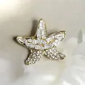 Spilla a forma di stella marina dorata con zirconi bianchi su sfondo di tessuto - Forma a stella marina / Oro