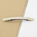 Pearlescent white acetate barrette with gold lettering on a minimalist cream background - Pearl White