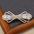 Elegante fermaglio per capelli a fiocco dorato con perle bianche e strass su sfondo grigio - Nastro