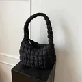 Bolso acolchado negro con textura de rejilla sobre una base de madera minimalista - Negro