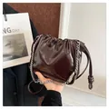 Close-up of glossy pleated handbag texture with silver chain strap and drawstring detail - Coffee