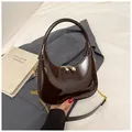 Dettaglio di una borsa hobo marrone scuro lucida con catena dorata su sfondo strutturato - Taglia unica / caffè