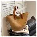 Minimalist straw woven tote bag with brown leather handles on a black leather sofa - Khaki