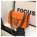 Leuchtend orangefarbene Tasche mit Schlangenhautmuster, Metallschließe und grauer Kette - Orange