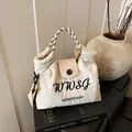 Minimalist cream tote bag with quilted texture and checkered handle on a vintage book - White