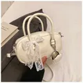 Detail of cream white handbag featuring a large lace bow and silver heart charm accessory - White With Pendant