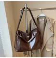 Detail van donkerbruine glanzende leren tote bag met fijne stiksels en metalen sluiting - Bruin