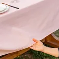 Detail of pink cotton tablecloth edge showing fabric texture and natural drape on wood table - Pink