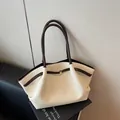 Cremefarbene Shopper-Tasche mit braunem Lederbesatz und goldener Schnalle auf einem Ständer - Cremeweiß