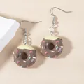 Close-up of chocolate-colored donut earrings with cream frosting and sprinkles on beige backdrop - Donut / Brown