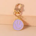 Detail of light purple enamel smiley face pendant with gold lobster clasp on sand background - Purple