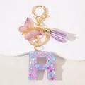Close-up of pink resin letter R keychain with sequins, butterfly charm and purple tassel - Letter R Purple Tassel