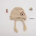 Detail of baby knit hat with brown bear patch and tassels on soft beige fabric - Baby One Size Elastic / Bear Khaki