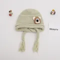 Close-up of light green knit baby hat with earflaps, tassels and cute bear patch - Baby One Size Elastic / Bear Light Green