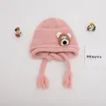 Detail of pink knitted baby hat with brown bear patch and tassels on soft gray background - Baby One Size Elastic / Bear Pink