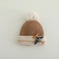 Detail van gebreide kindermuts met cartoonvliegtuigje en pluizige pompon van nepbont - Kinderen 2-8 Jaar / Lichtkoffie