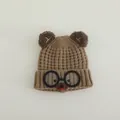 Detail of a brown knitted children's hat with bear ears and cartoon glasses decorations - Coffee