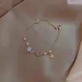Dettaglio del bracciale dorato con stella, luna, perle e fiocco su seta champagne - Bracciale Perla Zircone Stella Luna Blu