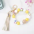 Detail of beaded keychain bracelet with wood beads, yellow silicone, and beige tassel charm - Yellow Daisy Print