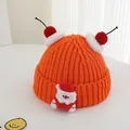 Detailed knit texture of orange winter hat with cherry pom-poms and Santa Claus patch - One Size / Orange