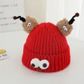 Close-up of red knit hat featuring plush googly eyes and black spiral tentacles - Red