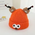 Close-up of bright orange monster knit hat with plush antennas and cartoon eye details - Orange