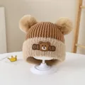 Close-up of knit baby bear earflap hat with dual pom-poms and cute cartoon patch - Style 1 Coffee