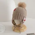 Detail of baby knit earflap hat with soft pompom and floral patch on khaki ribbed fabric - Children Elastic Style / Brown