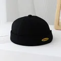 Dettaglio del berretto docker nero con placca in metallo dorato KUKUJI e bordo risvoltato - 50-52cm / Nero
