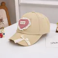 Detail van beige kinderpet met rood geruit hart en een witte kanten strik als decoratie - 48-52cm / Khaki