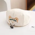 Detailed close-up of cream cotton baby cap with bear embroidery and adjustable drawstring - Toddler Size / Beige