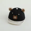 Detail view of plush bear ears and embroidered face on a black and white baby baseball cap - Toddler One Size / Black