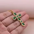 Hand holding a gold cross pendant necklace with green emerald stones and micro zircons - Green