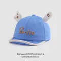 Detail van blauwe baby pet met Smile borduursel en zachte cartoon beertje oortjes erop - Baby Maat / Blauw