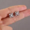Elegante Kleeblatt-Ohrstecker aus Silber mit Zirkonia-Steinen auf der Hand präsentiert - Silber